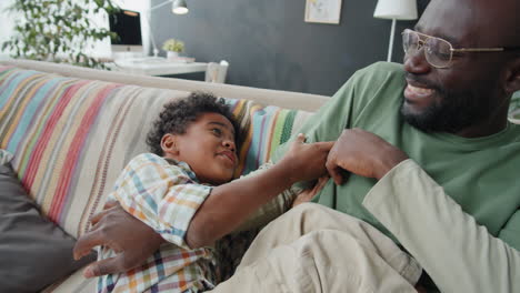 Joyous-African-American-Man-Tickling-Little-Son-on-Sofa-at-Home
